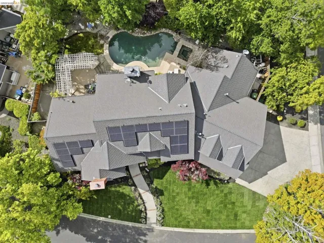 Expansive residential property featuring a gray shingled roofline, multiple solar panel arrays, a curved concrete paver walkway, and a manicured front lawn