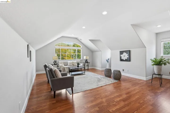 Spacious room featuring vaulted ceilings, wood-finish flooring, recessed lighting, and a large arched window