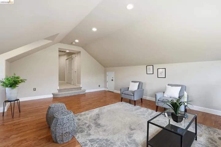 Spacious finished attic featuring wood-finish flooring, recessed lighting, sloped ceilings, and a carpeted landing with two panel doors