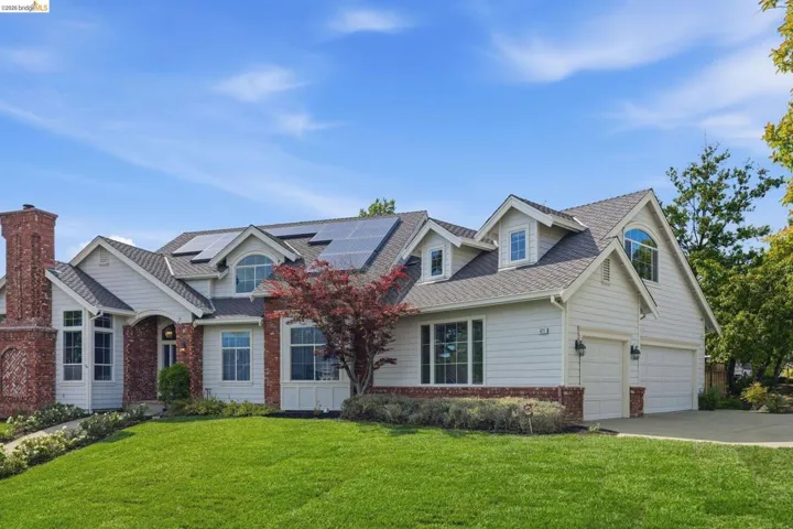 Traditional-style residence featuring white siding, red brick accents, dormer windows, and a multi-car garage with individual doors