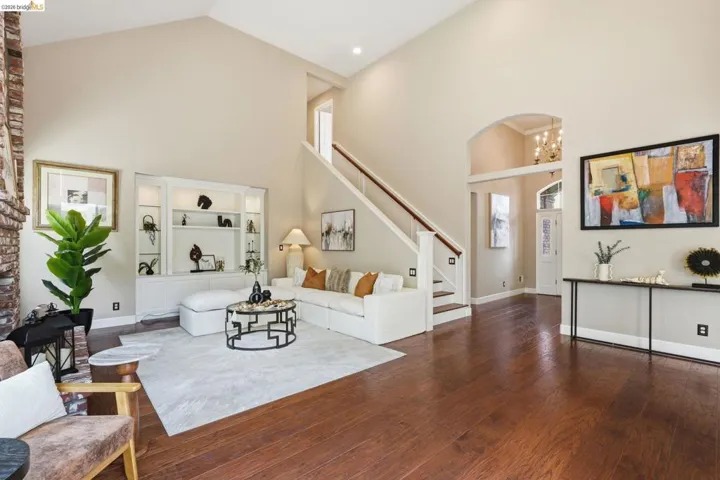 Vaulted ceilings above rich wood-finish flooring, a built-in media center with integrated lighting, and a brick-finish fireplace