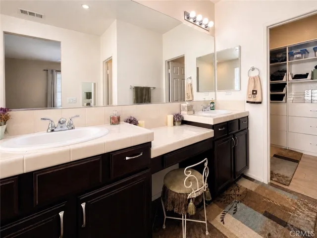 Primary ensuite bathroom with dual sinks, dressing table, and entrance to large walk-in closet