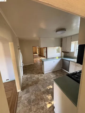 Kitchen with a peninsula, stainless steel dishwasher, freestanding refrigerator, black gas cooktop, and light countertops