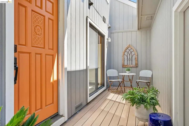 Inviting exterior entrance featuring a vibrant orange paneled door with decorative detailing, vertical siding, and a private outdoor deck area