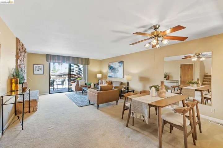 Open-concept living area featuring a stone accent wall, sliding glass door to an outdoor patio, ceiling fan with integrated lighting, and neutral carpeting