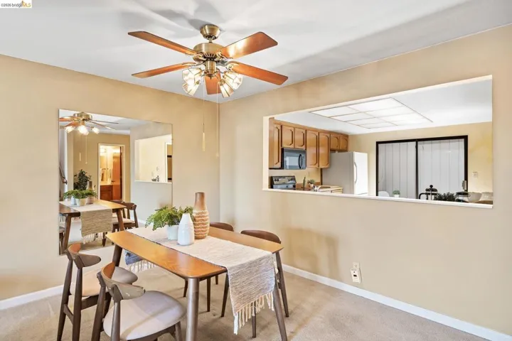 Dining area featuring a pass-through window to the kitchen, a ceiling fan with integrated lighting, and carpet flooring