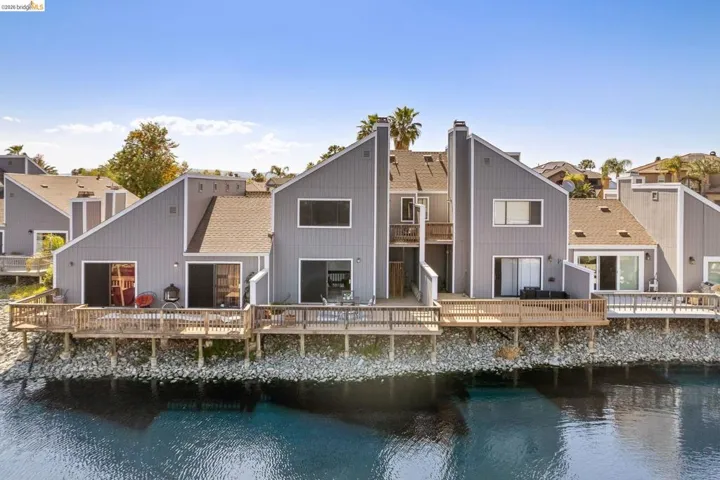 Waterfront property featuring multiple private decks, sliding glass doors, and a contemporary architectural design with gabled roofs