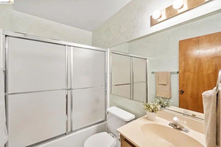 Bathroom featuring a shower/tub combination with sliding frosted glass doors, a vanity with an integrated sink, a large wall-mounted mirror, and overhead strip lighting