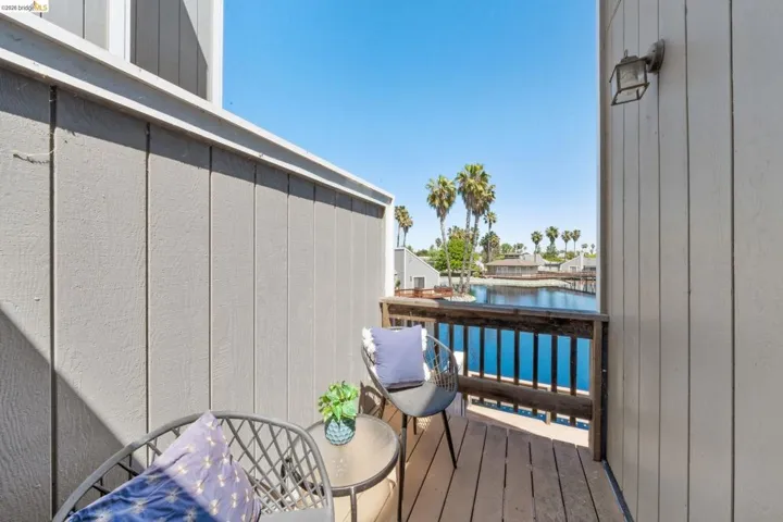 Private balcony featuring wood-finish decking, a robust wood railing, exterior lighting, and water frontage with palm tree landscaping