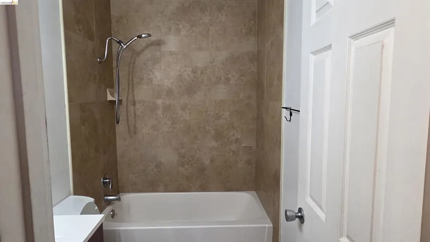 Bathtub with tiled surround, chrome shower fixtures, and a multi-panel door