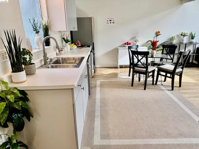 Kitchen area featuring white cabinetry, a stainless steel sink with a gooseneck faucet, light-toned countertops, and wood-finish flooring