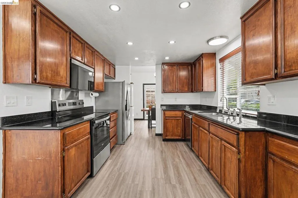 Kitchen featuring wood-finish cabinetry, black countertops, and light wood-look flooring