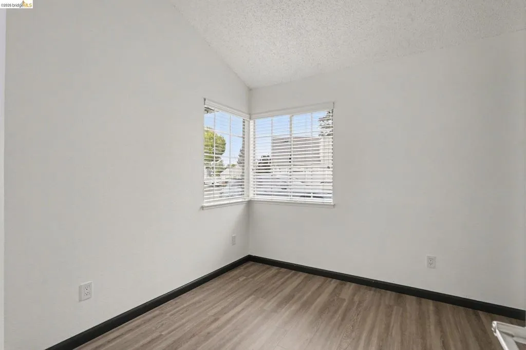 Corner window configuration with white blinds, wood-finish flooring, white walls, dark baseboards, and a vaulted ceiling
