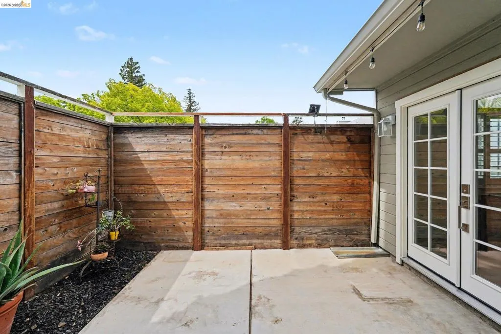 Private outdoor patio space featuring concrete paving, dark ground cover, and natural wood privacy fencing