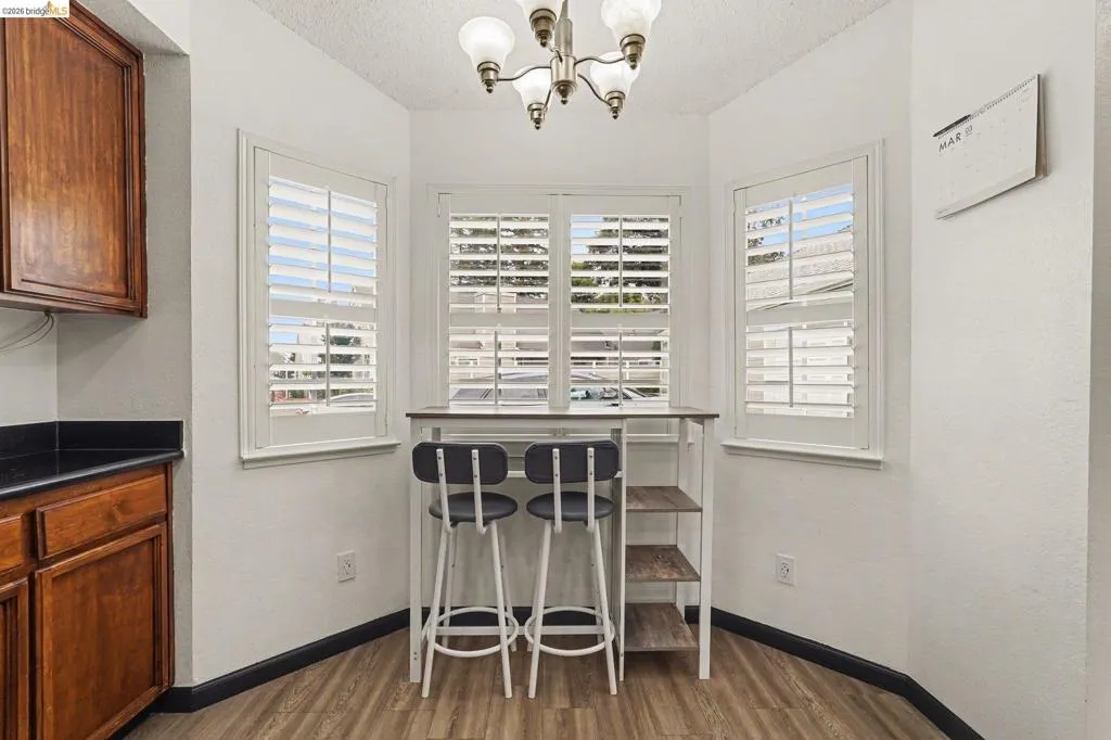 Breakfast nook featuring three windows with white plantation shutters, wood-finish flooring, and a brushed nickel chandelier