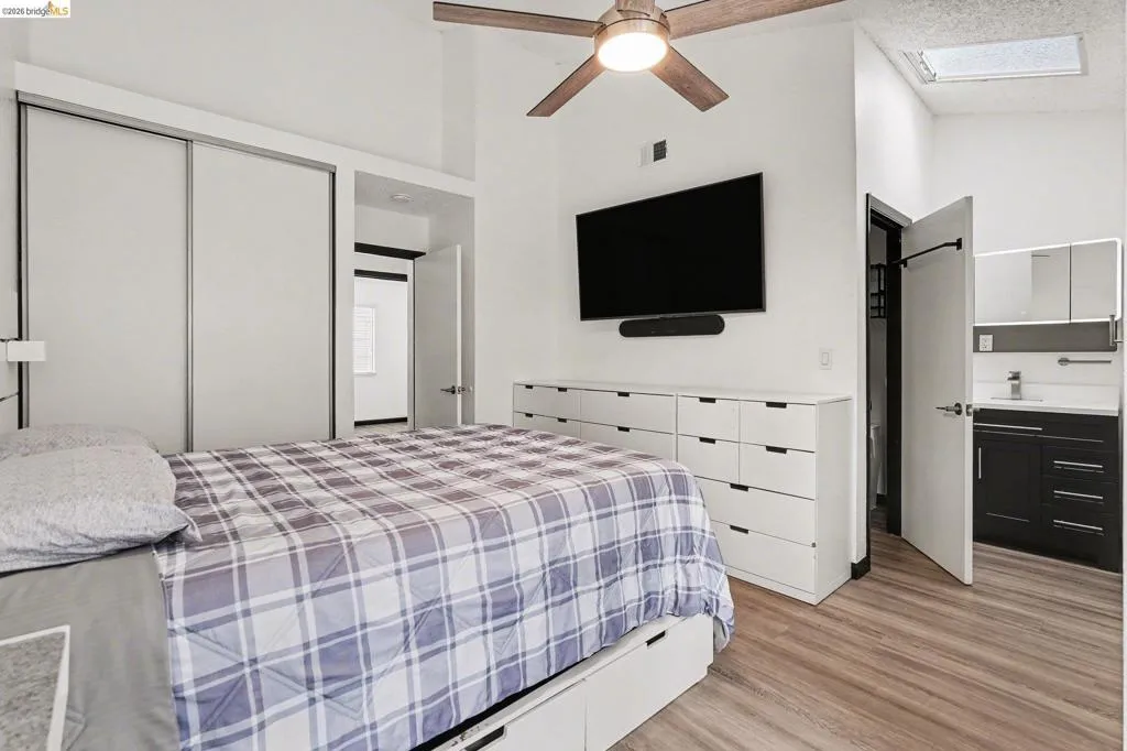 Vaulted ceiling with an integrated ceiling fan, light wood-finish flooring, and a skylight