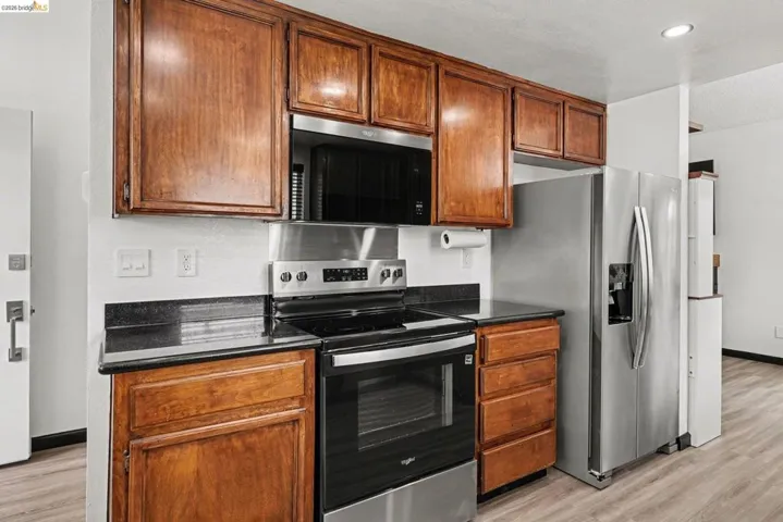 Kitchen featuring wood-finish cabinetry, black countertops, stainless steel appliances, and wood-finish flooring