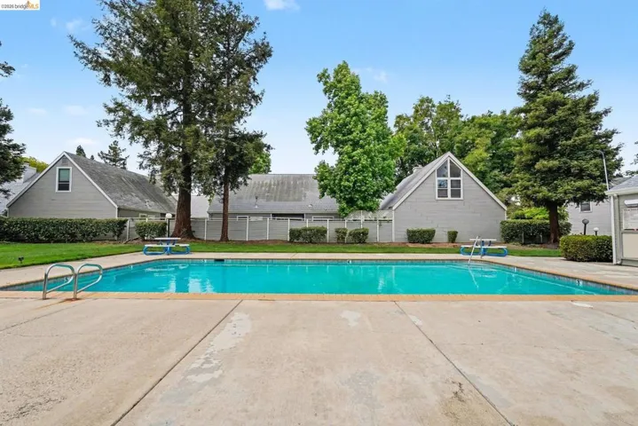 Community swimming pool with concrete decking, surrounding green lawn, and mature trees