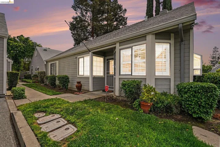 Exterior featuring light gray horizontal siding, bay windows with white frames, a covered entry, and a gabled roofline