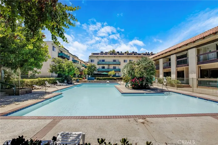 View of the gated pool area, beautifully framed by lush trees and vibrant flower landscaping. The well-maintained grounds create a serene, private retreat within the condo community.