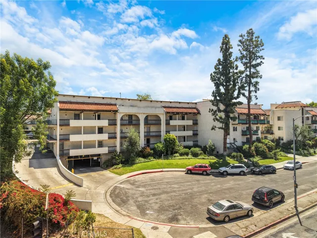 Front view of the three-story condo building at the end of a cul-de-sac, as seen from the main street. The first-floor unit includes access to an underground garage. Mature trees, well-kept landscaping, and a desirable neighborhood location enhance the cul-de-sac setting.