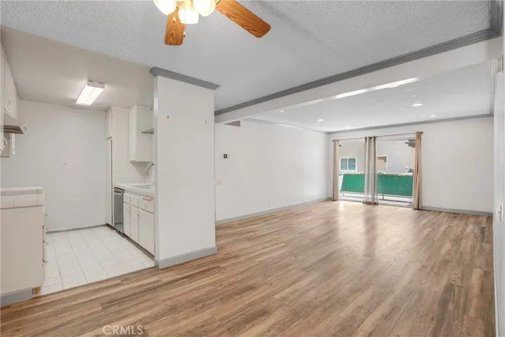 View of the living room looking out toward the balcony, with the kitchen visible in the background. The layout offers a comfortable flow between living, dining, and outdoor spaces.