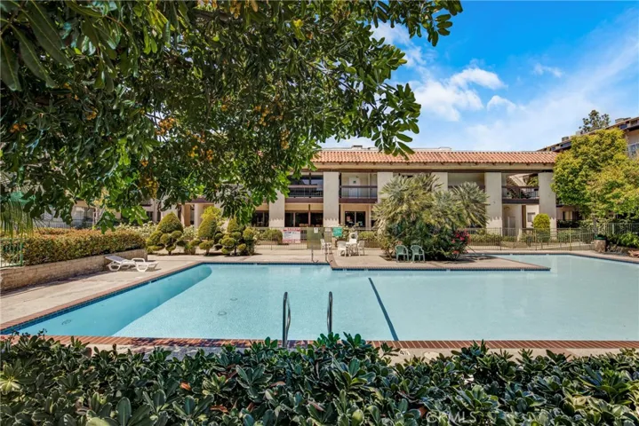 View of the gated pool area, beautifully framed by lush trees and vibrant flower landscaping. The well-maintained grounds create a serene, private retreat within the condo community.