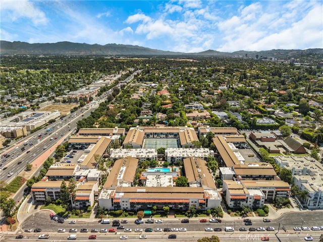 Full aerial view of the condo community, showcasing the entire building and its surrounding grounds. The layout highlights the pool, tennis courts, and proximity to the neighborhood.