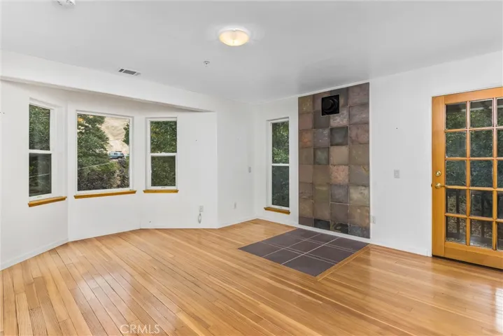 Original Image- Bedroom #1. This photo might make the floor appear wavy. It isn't. Solid wood flooring, an area prepared for a Franklin Stove, windows to enjoy the tree view, a door to an exterior deck