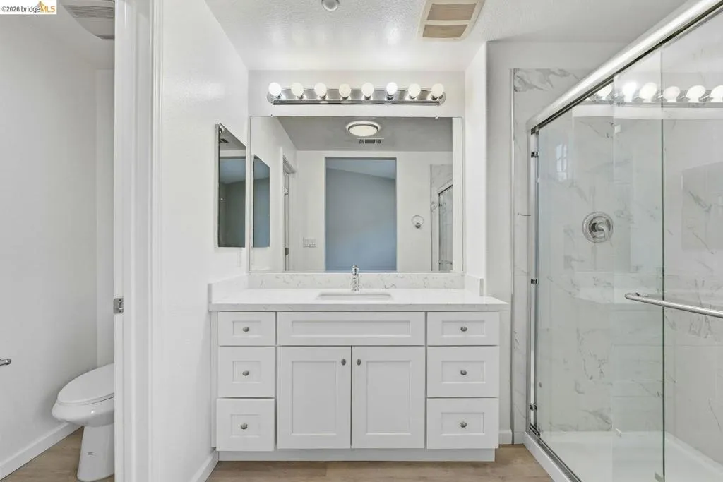full bath featuring vanity, a marble finish shower, and light wood-style flooring