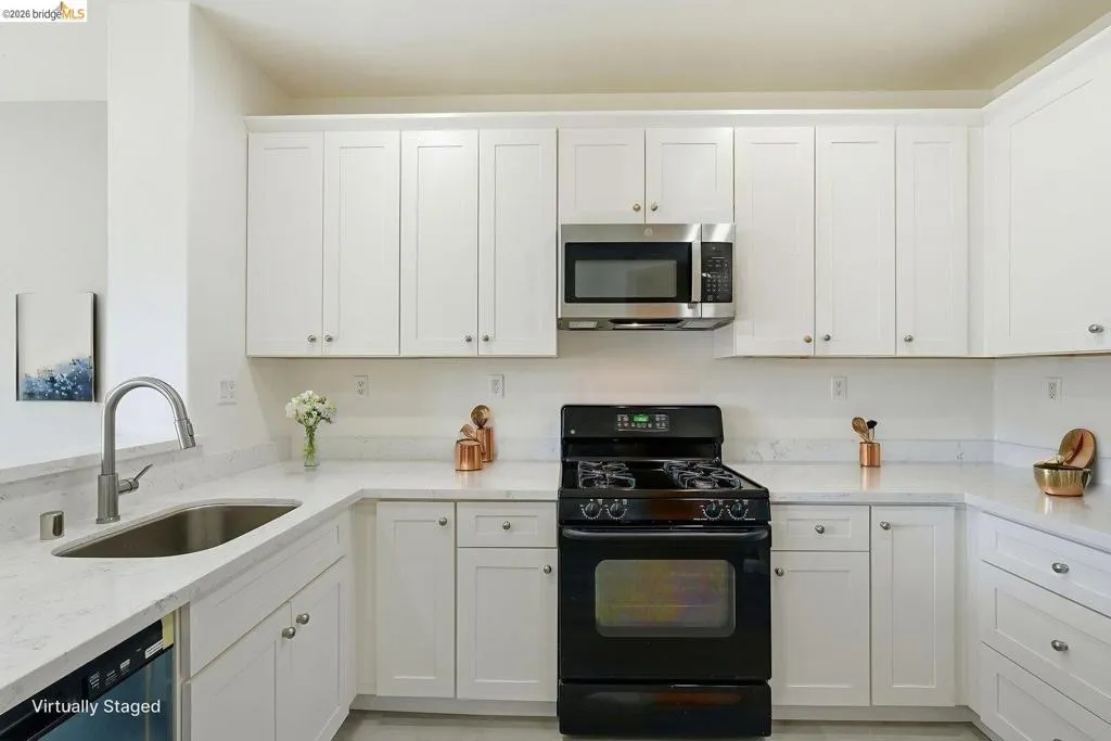 kitchen with black range with gas cooktop, white cabinetry, light stone counters, and stainless steel microwave