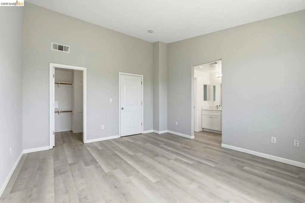 unfurnished bedroom with light wood-type flooring, a spacious closet, and ensuite bathroom