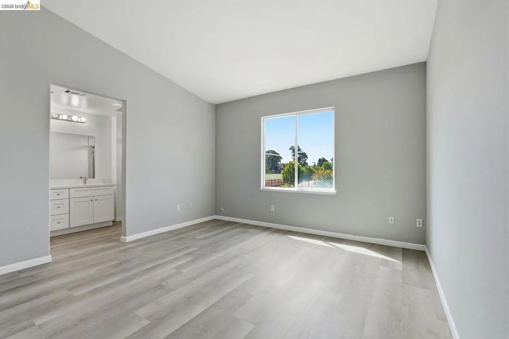 unfurnished bedroom featuring vaulted ceiling, light wood-type flooring, and connected bathroom