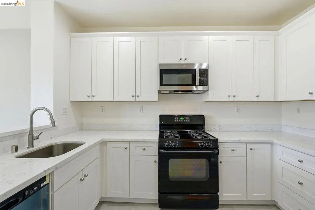 kitchen with black gas range oven, light stone countertops, white cabinets, stainless steel microwave, and dishwasher