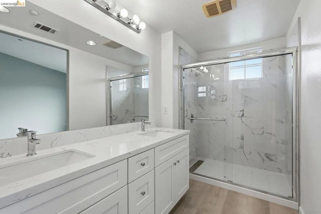 full bathroom with double vanity, plenty of natural light, a marble finish shower, and light wood-style floors