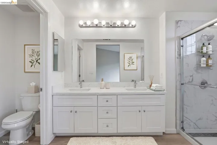 bathroom featuring double vanity, a marble finish shower, and light wood finished floors - Virtual Staging