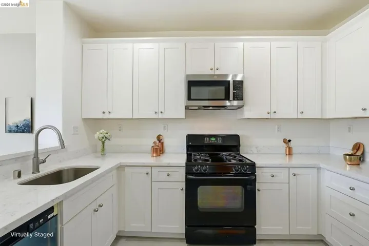 kitchen with black range with gas cooktop, white cabinetry, light stone counters, and stainless steel microwave