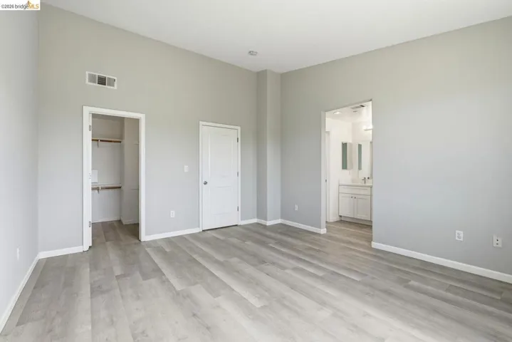 unfurnished bedroom with light wood-type flooring, a spacious closet, and ensuite bathroom