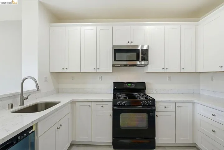 kitchen with black gas range oven, light stone countertops, white cabinets, stainless steel microwave, and dishwasher