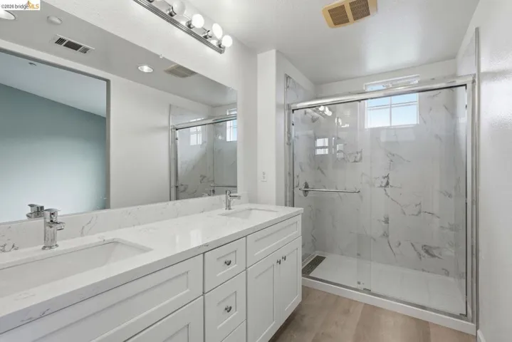full bathroom with double vanity, plenty of natural light, a marble finish shower, and light wood-style floors