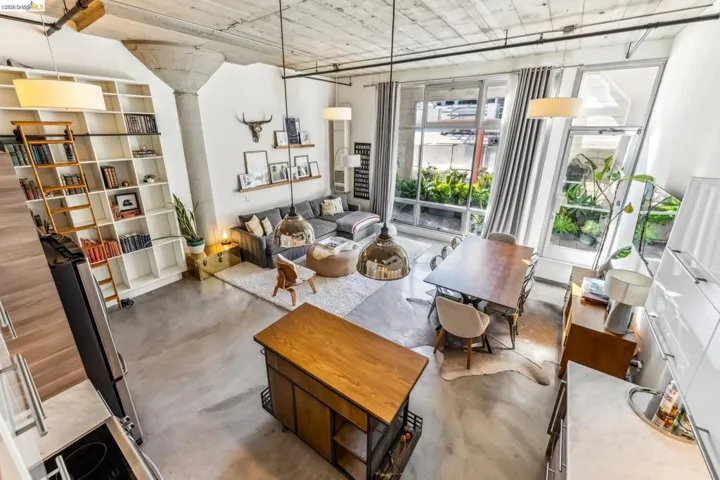 Open-concept living space featuring high ceilings with exposed concrete, extensive industrial-style windows, polished concrete flooring, a large built-in bookshelf with a rolling ladder, and a kitchen island with a wood countertop