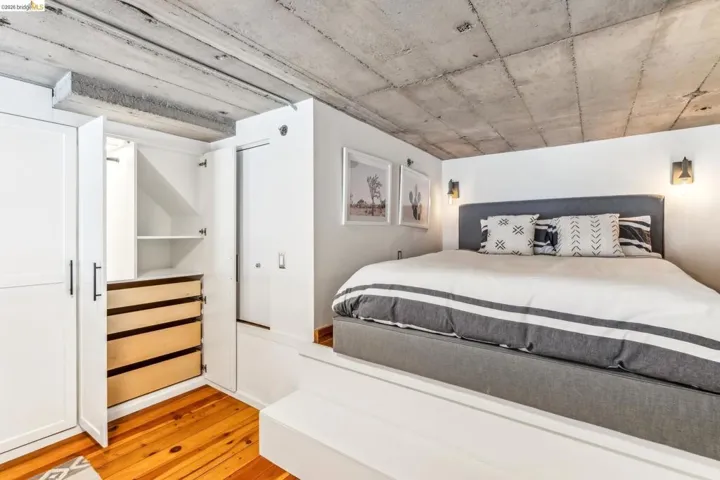 Built-in cabinetry with multiple drawers and shelving, concrete ceiling, hardwood flooring, wall-mounted sconce lighting, and a raised platform