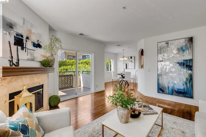 Living area featuring wood-finish flooring, a fireplace with a stone surround and wood mantel, and sliding glass doors opening to a private balcony