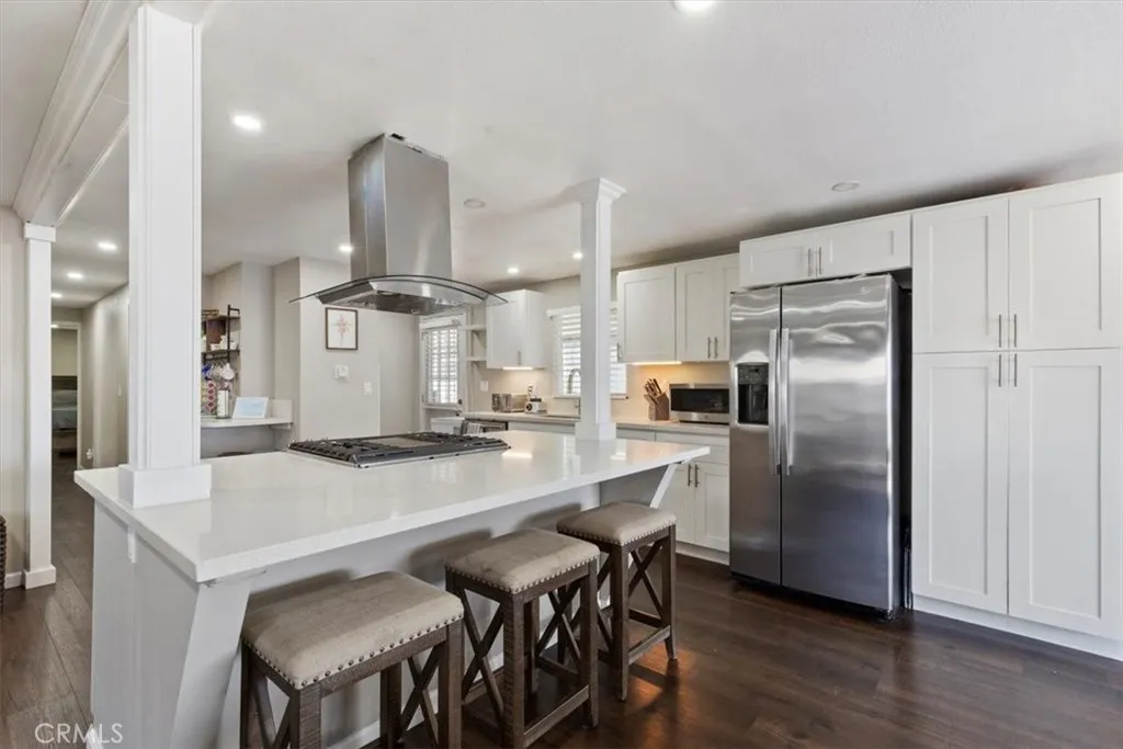 Updated Kitchen: Open island kitchen with white cabinetry, stainless steel appliances, bar seating, recessed lighting, and seamless flow to the living and dining areas.
