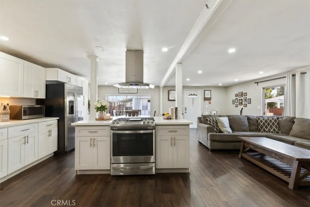 Updated Kitchen: Open island kitchen with white cabinetry, stainless steel appliances, bar seating, recessed lighting, and seamless flow to the living and dining areas.