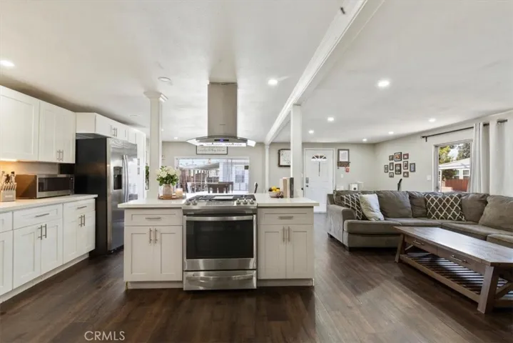 Updated Kitchen: Open island kitchen with white cabinetry, stainless steel appliances, bar seating, recessed lighting, and seamless flow to the living and dining areas.
