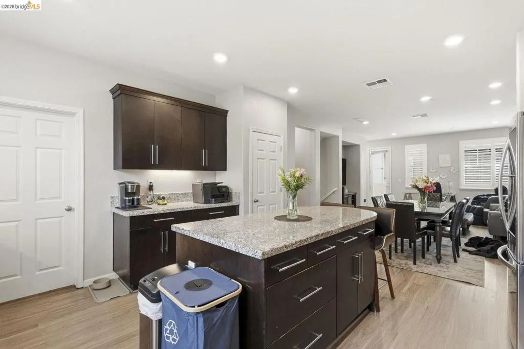 kitchen with a kitchen island, a kitchen breakfast bar, dark wood finish cabinetry, light stone countertops, and recessed lighting
