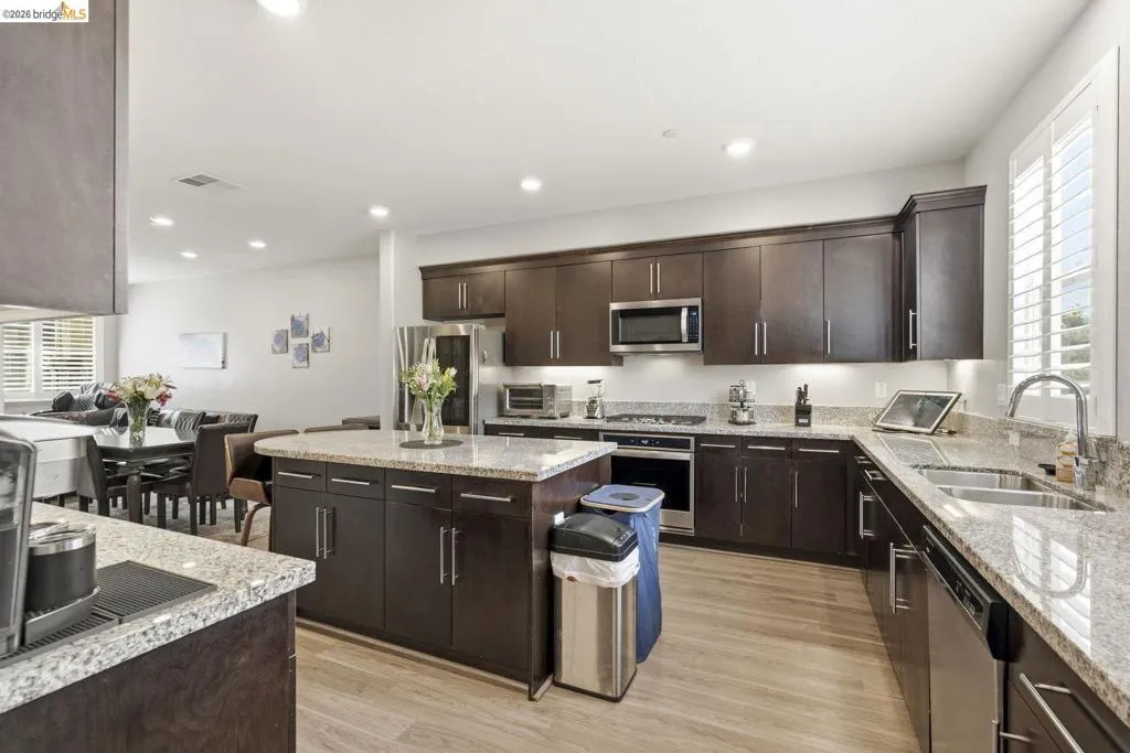 kitchen featuring a center island, dark wood finish cabinetry, stainless steel appliances, light stone countertops, and light wood finished floors
