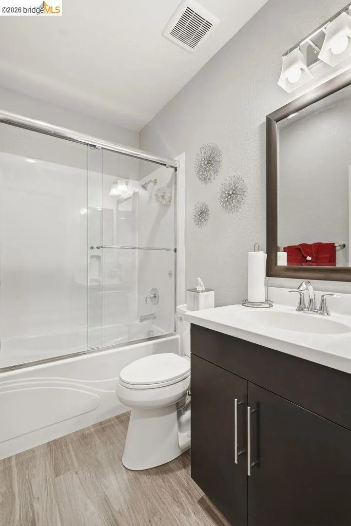 full bathroom with vanity, light wood finished floors, combined bath / shower with glass door, and a textured wall