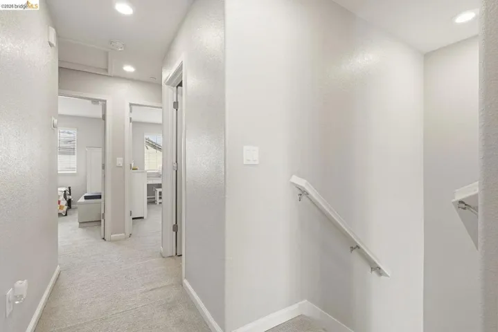 hall with light colored carpet, recessed lighting, a textured wall, and an upstairs landing